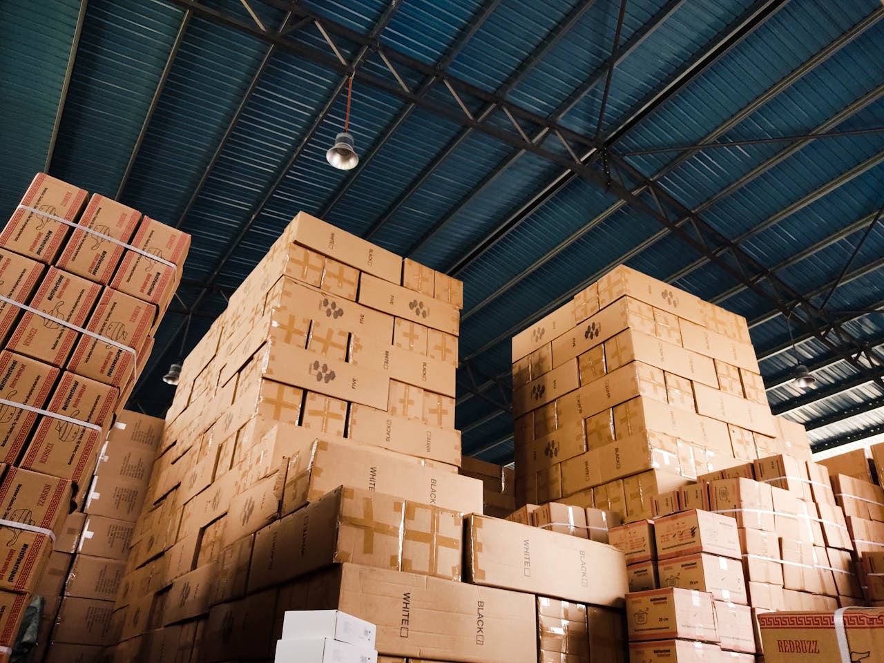 about-01 High stacks of cardboard boxes organized in a warehouse with a blue metal ceiling.
