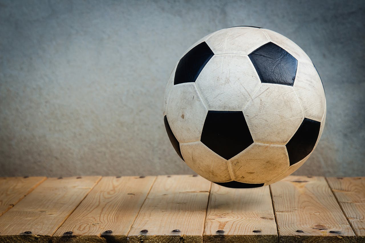 cta-bg Vintage soccer ball resting on wooden planks against a textured background, symbolizing sports tradition.