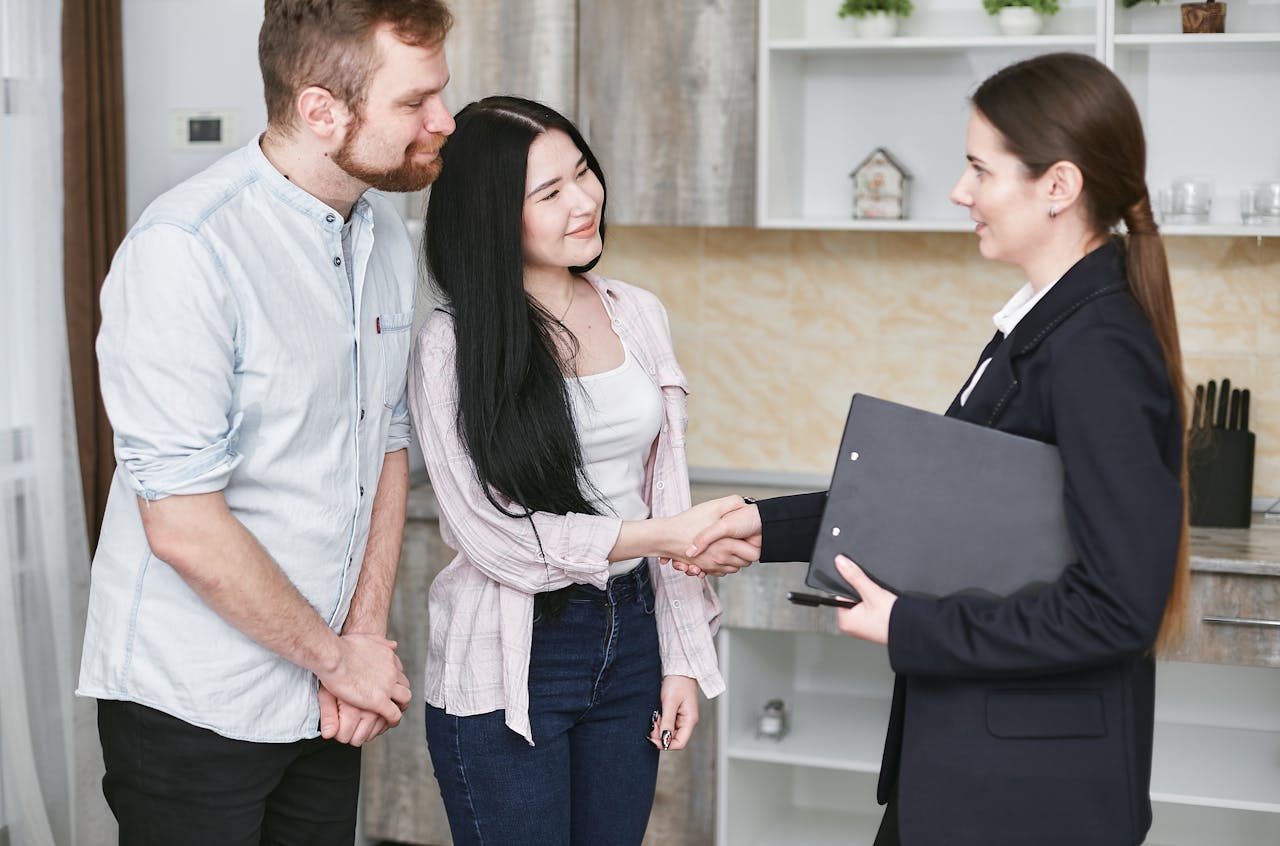 home-services-01 A young couple shakes hands with a real estate agent during a home tour or negotiation in a modern setting.